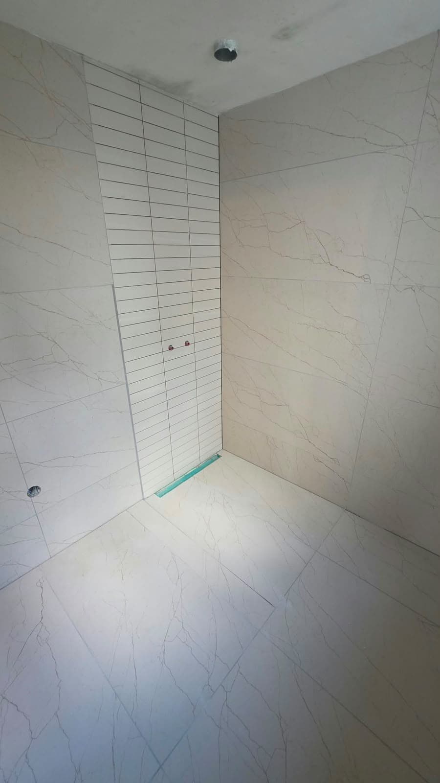 Tiling in a walk-in shower with large tiles, a strip of narrow tiles and a linear drain