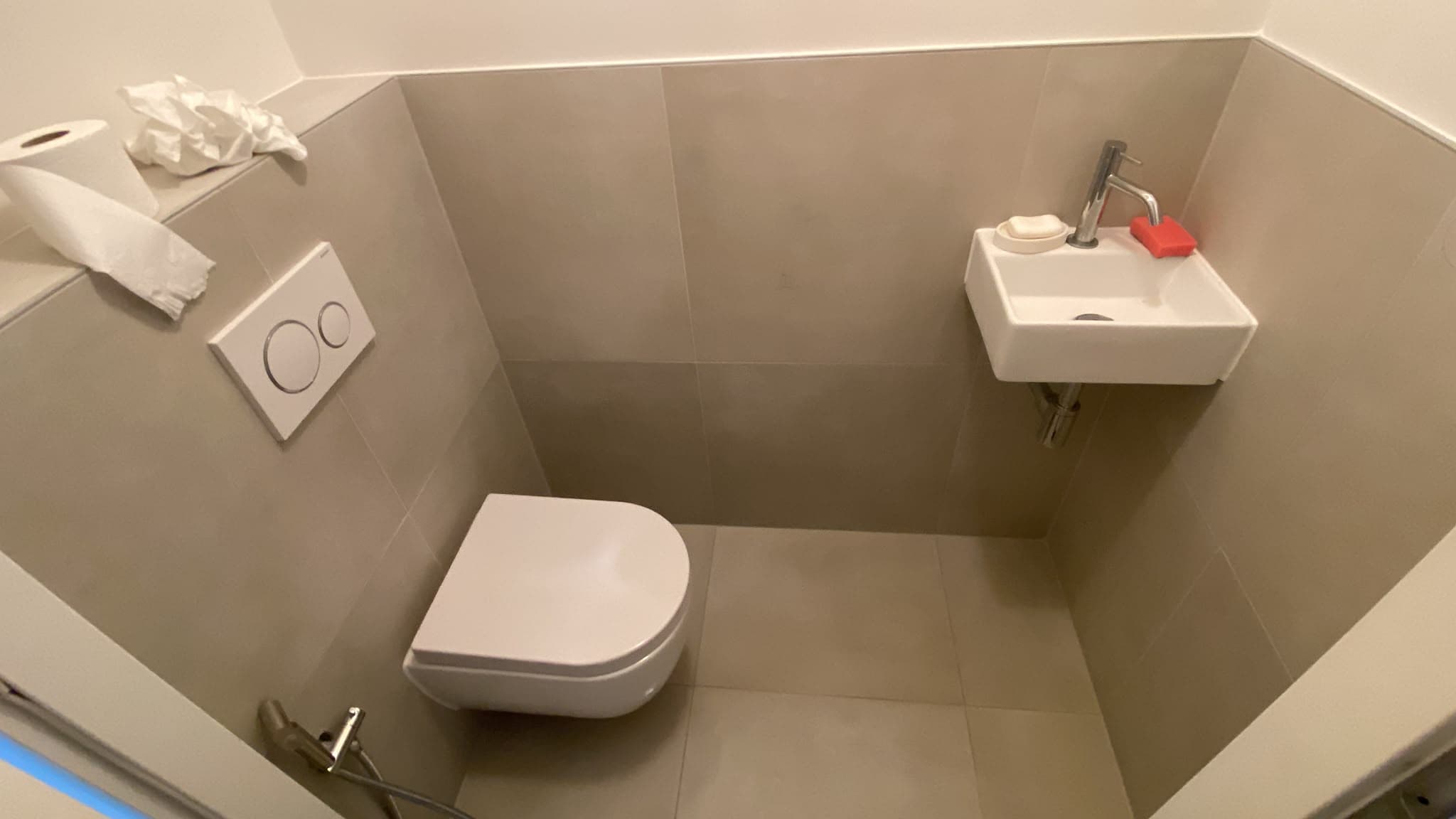 Renovated toilet with wall-hung toilet, small hand basin and large tiles